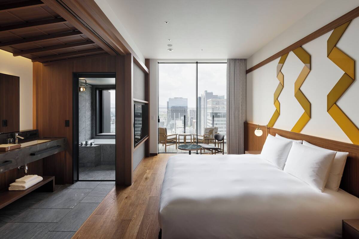 Une chambre d’hôtel avec un grand lit, une coiffeuse en bois, une salle de bain avec baignoire et un balcon offrant une vue sur la ville.