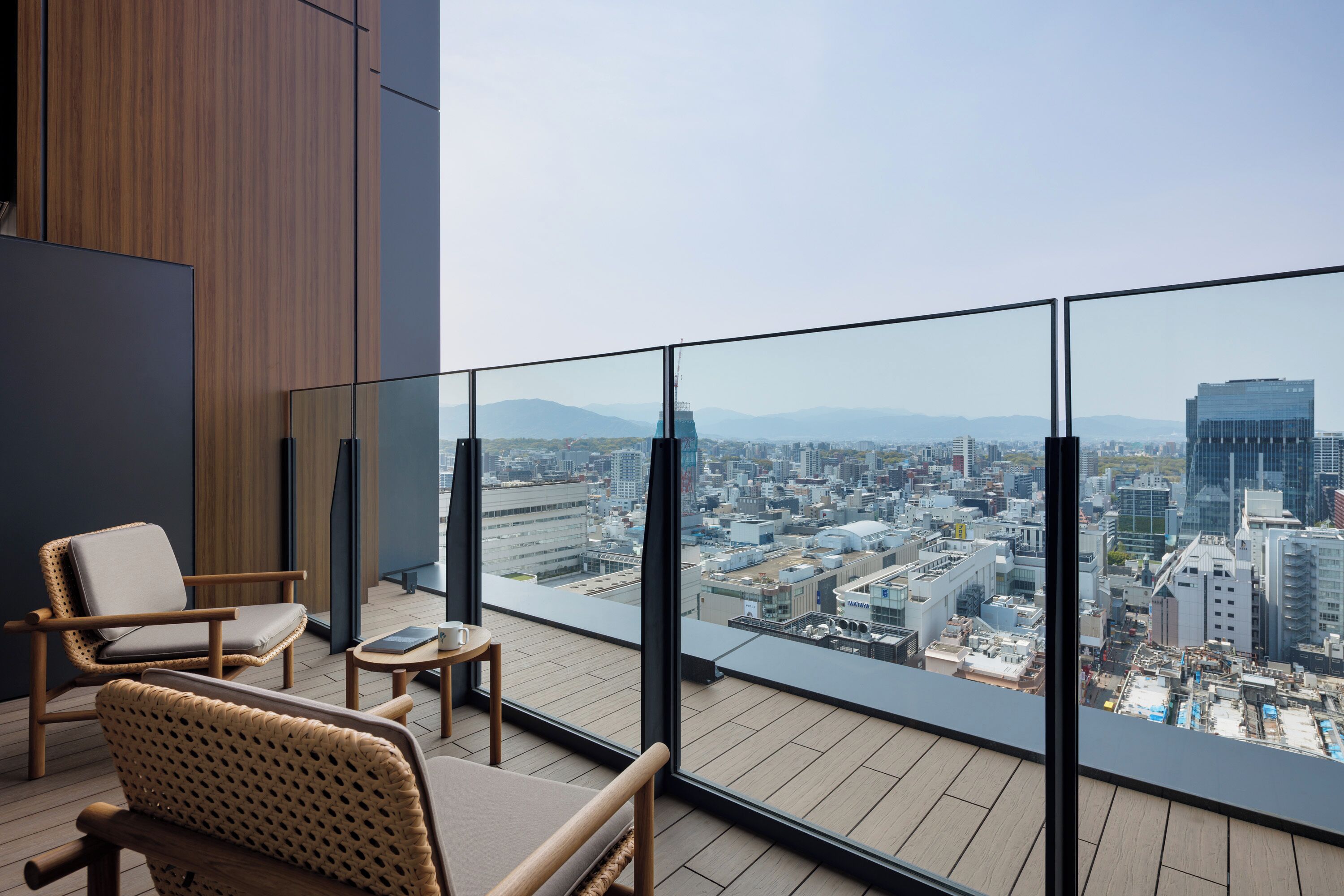 A modern room with a city view, featuring a balcony with wicker chairs and a small table.