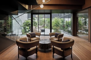 Un interior moderno con una pared de vidrio, dos sillones de cuero, una mesa redonda y vistas al exterior con vegetación.