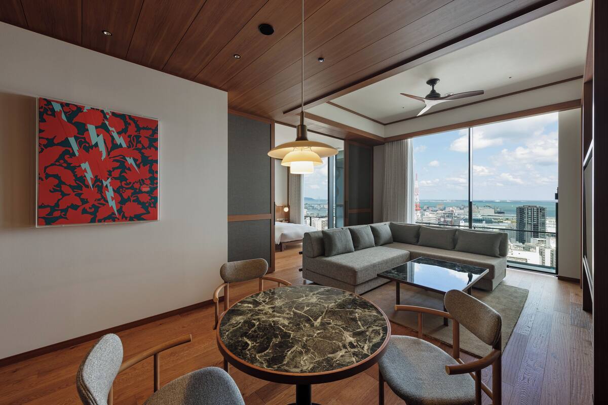 Une chambre d’hôtel moderne avec une table à manger en marbre, un canapé gris et une grande fenêtre donnant sur la ville.