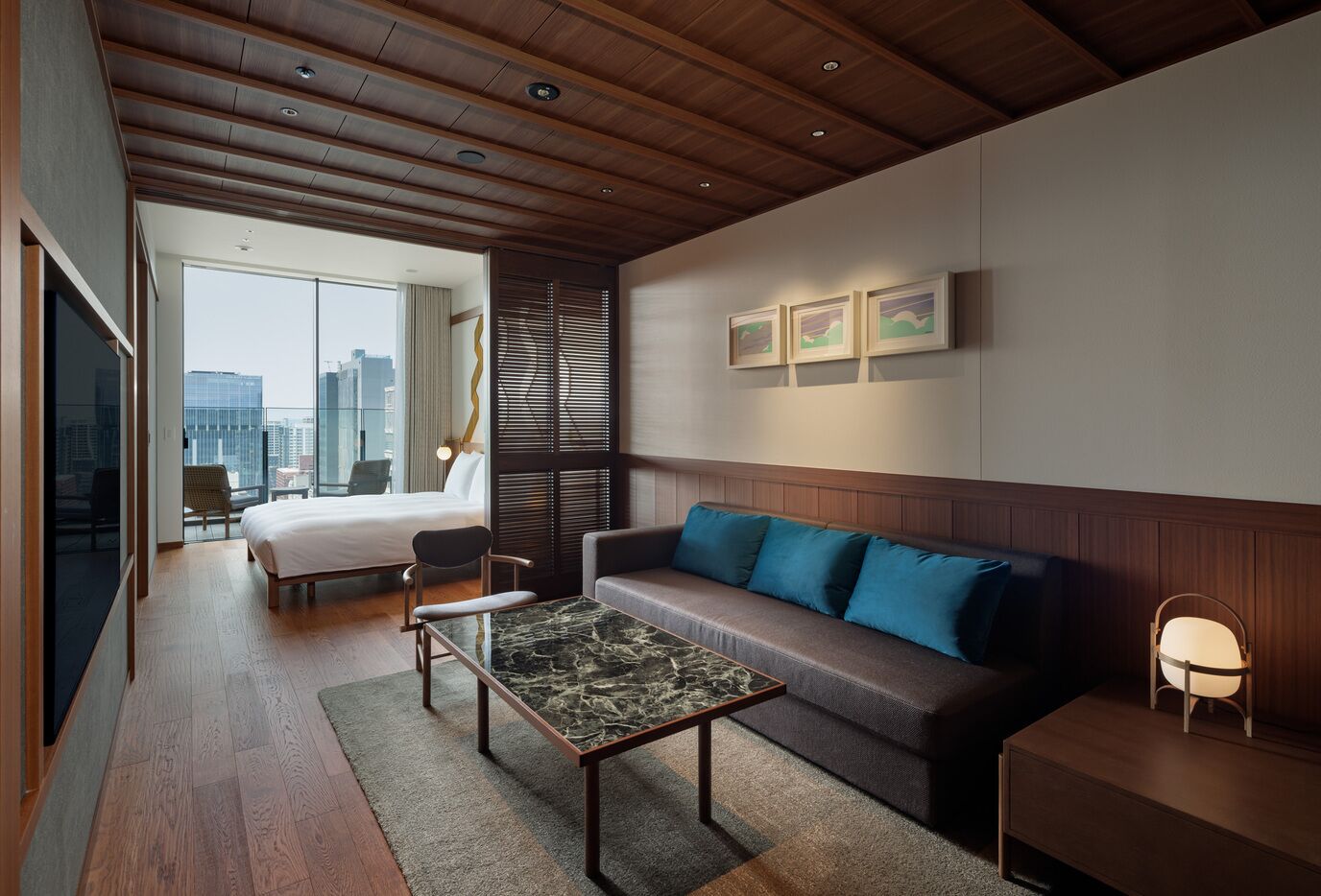 A modern hotel room with a bed, sofa, coffee table, and a view of the city.