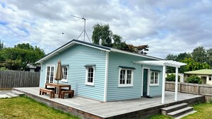 Ein hellblaues Haus mit überdachter Terrasse, einer Holzterrasse und einer Satellitenschüssel.