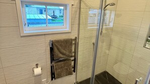 Ein modernes Badezimmer mit Toilette, einer in Glas abgeschlossenen Dusche, einem Fenster mit Blick auf ein Haus und einem Handtuchhalter mit zwei Handtüchern.