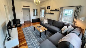 Ein Wohnzimmer mit Sofa, Couchtisch und Kamin. Eine Kristallleuchter, ein Spiegel und ein Fenster mit Vorhängen sind ebenfalls zu sehen.