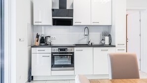 Une cuisine moderne avec des meubles blancs, un four encastré, une machine à café et un four à micro-ondes.