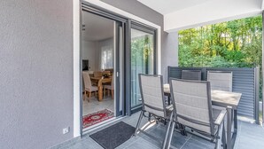 Un espace repas extérieur moderne, doté d’une porte vitrée donnant sur une salle à manger, d’une table en bois et de deux chaises.