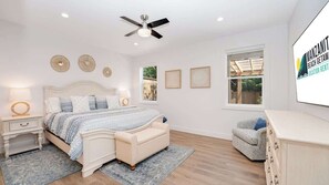 A bedroom with a bed, bedside tables, a ceiling fan, a window, and a wall-mounted TV.