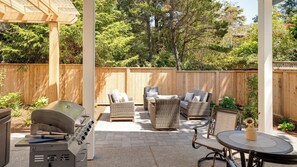 An outdoor patio with a grill, wicker furniture, and a round table.