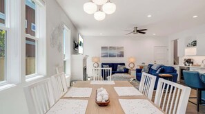 A modern living room with a dining table, sofas, and a kitchen area.