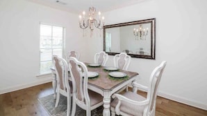 Comedor con mesa de madera, sillas blancas, candelabro y un espejo grande en la pared.