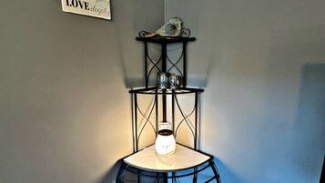 A corner room with a black metal shelf holding a vase and a decorative item, a wall-mounted sign with motivational text, and a power outlet.