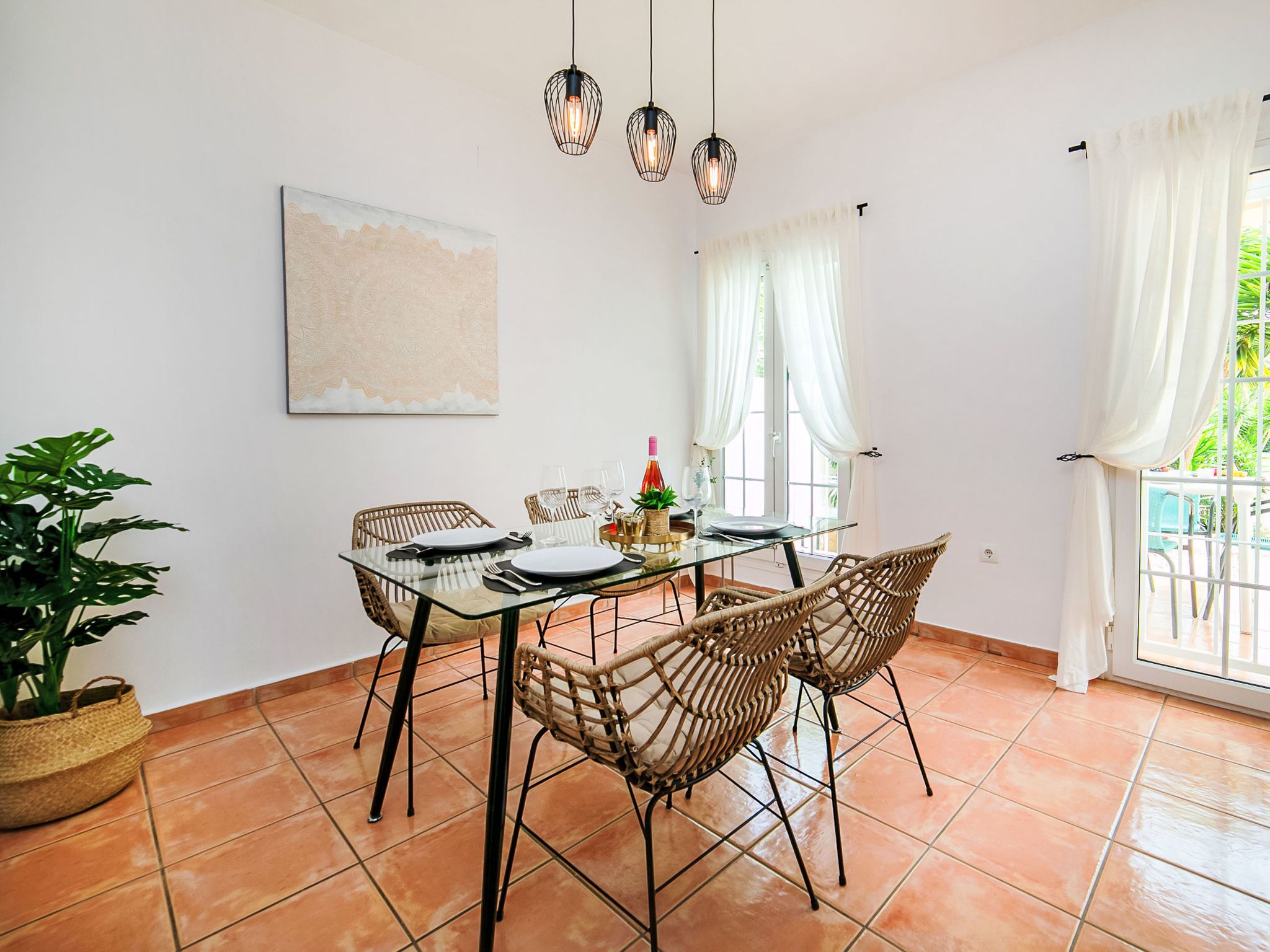 Un coin repas avec une table en verre, des chaises en osier et une plante en pot.