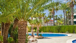 Zona de piscina con palmeras, sillones de descanso y un cielo azul despejado.
