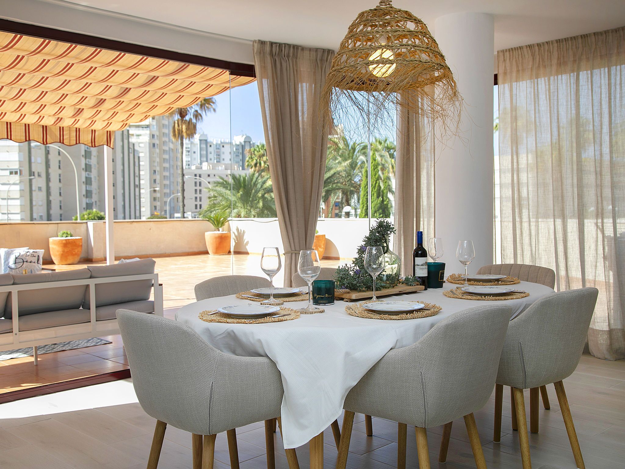 Comedor con una mesa preparada para cuatro personas, con individuales tejidos y una botella de vino.