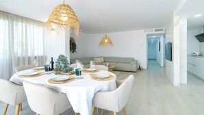 Un comedor moderno con una mesa redonda dispuesta para seis personas, sillas blancas y dos lámparas colgantes de mimbre.