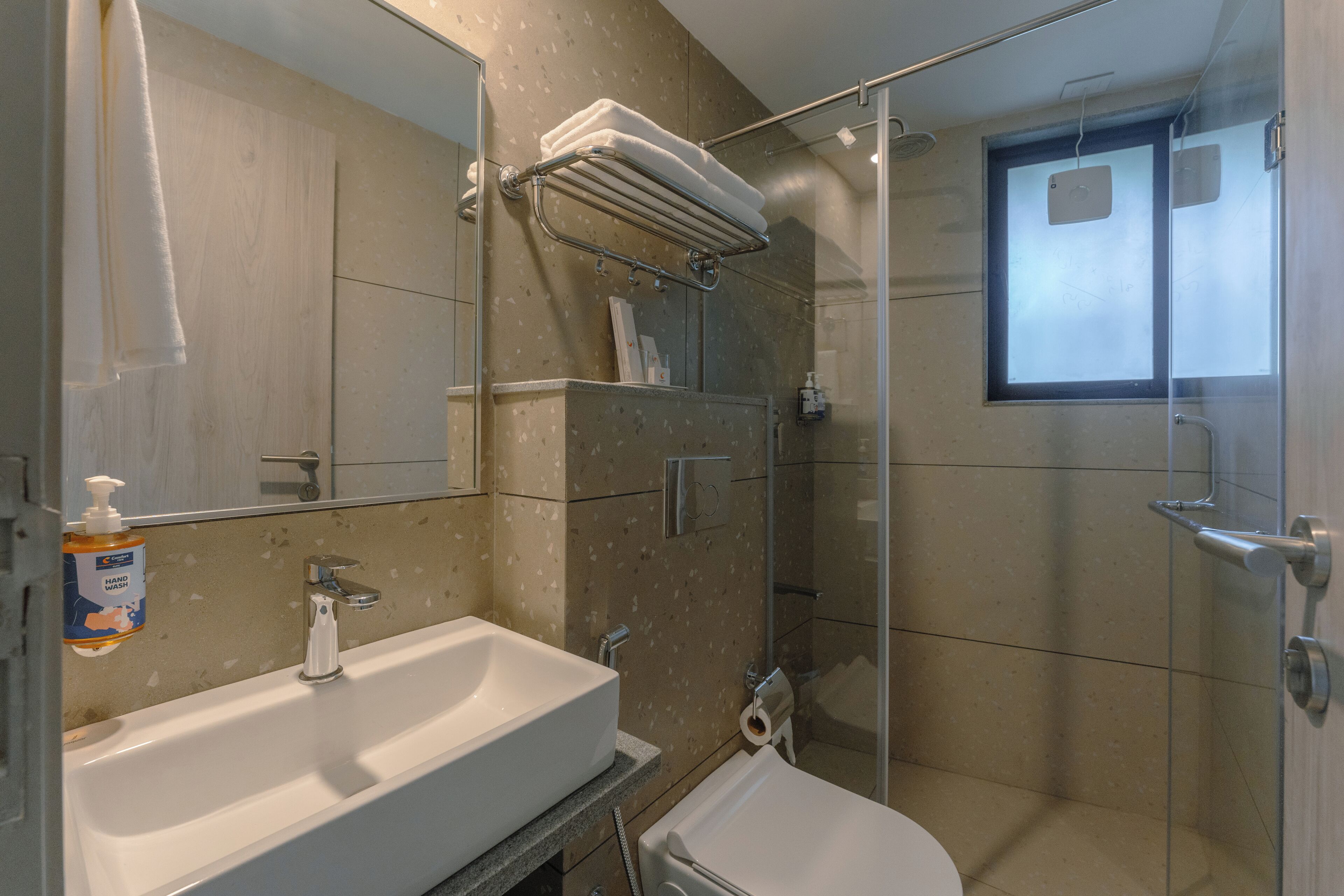 A modern bathroom with a sink, mirror, towel rack, shower, and toilet.