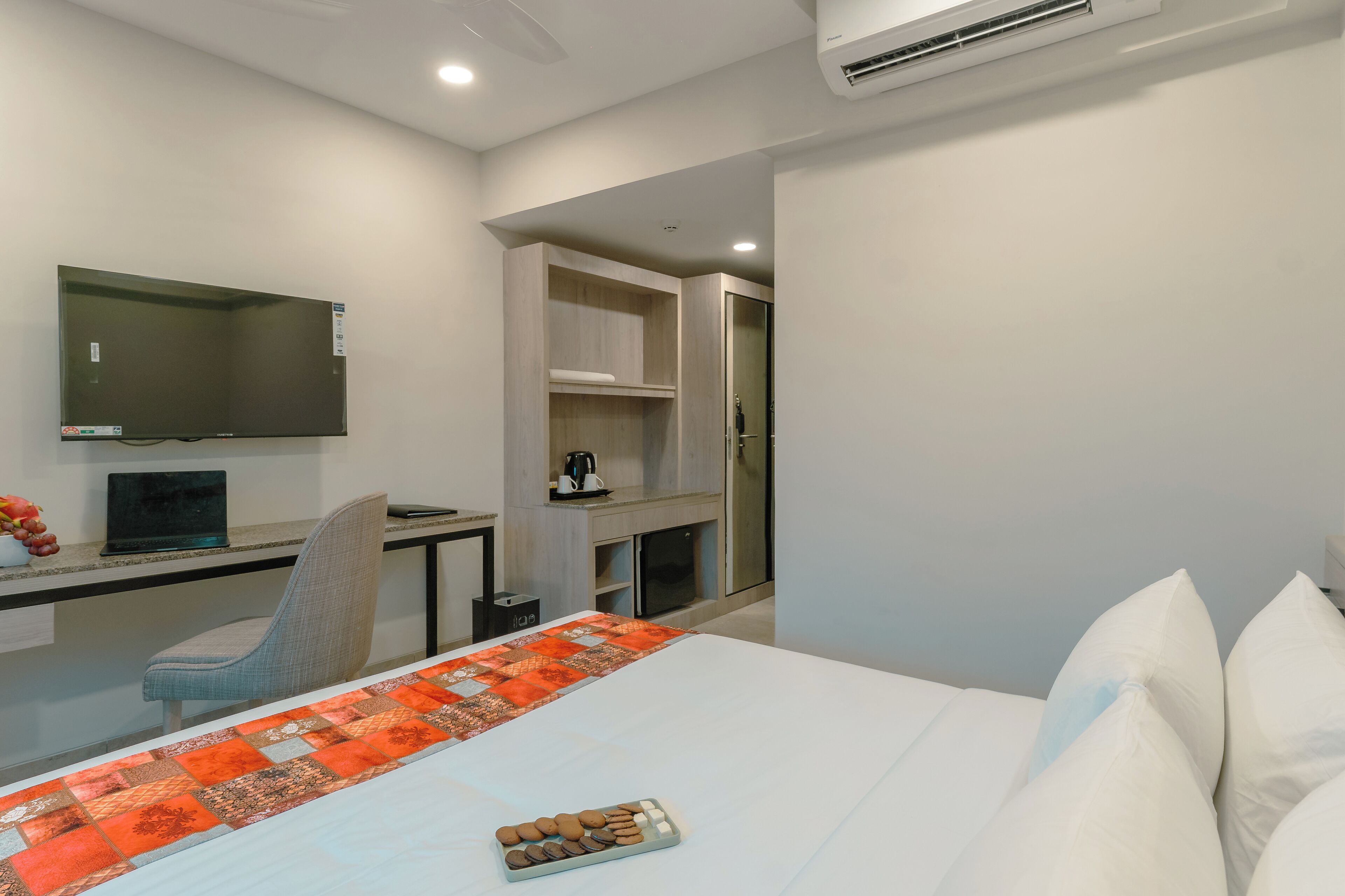 A modern hotel room with a large bed, a desk with a laptop, a chair, and a TV mounted on the wall.