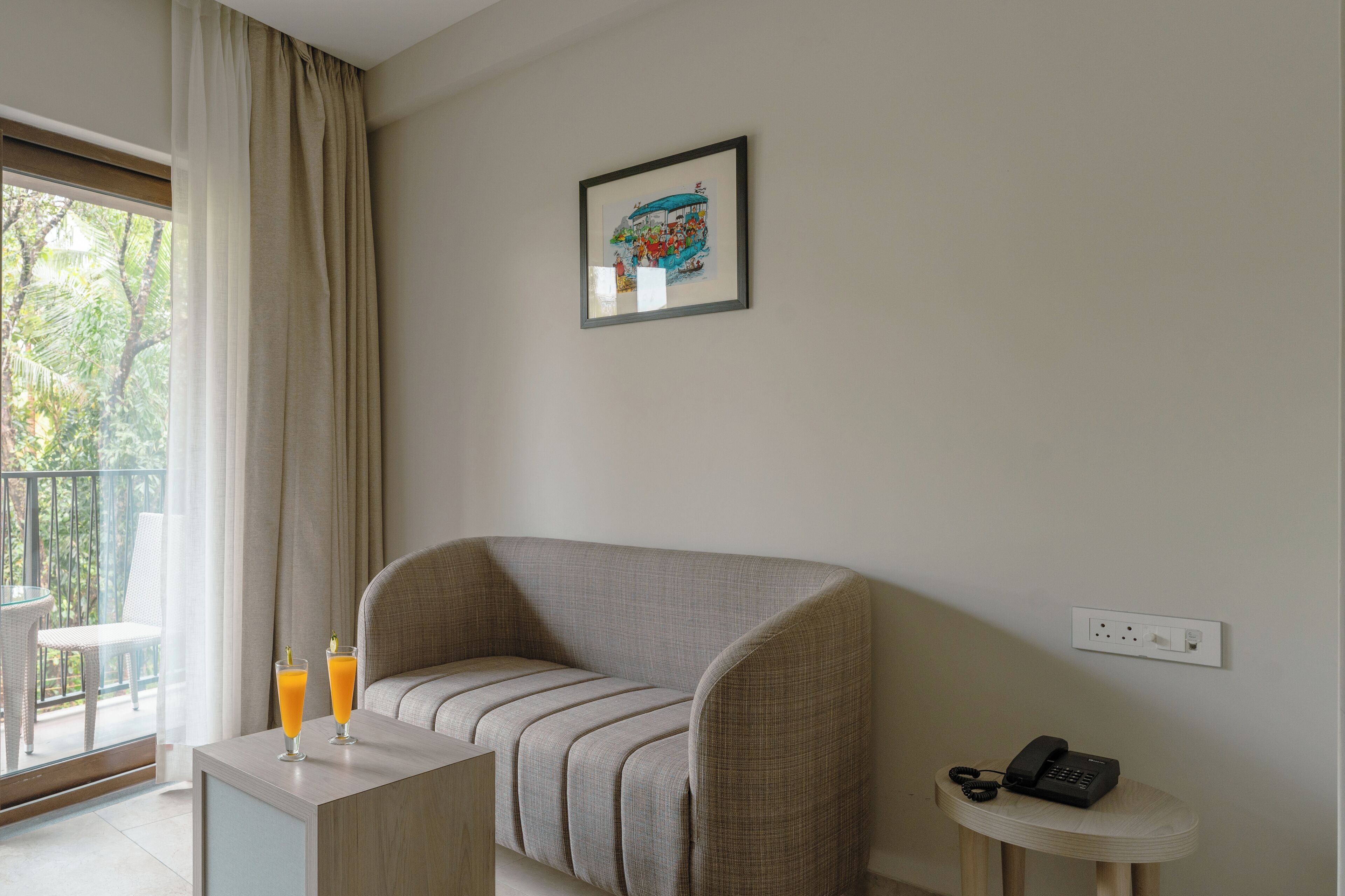 A modern hotel room with a sofa, a small table with two glasses of orange juice, a framed picture on the wall, and a phone on a side table.