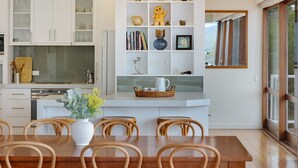 Een moderne keuken met witte kasten, een centraal eiland met een mand, en een eethoek met houten stoelen en een tafel.