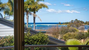 A view from a balcony overlooking a beach with palm trees, boats, and a clear sky. - Baywatch 3 - Best Location & A View! (Merimbula)