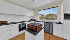 A modern kitchen with white cabinets, a wooden island, and a large window. - Cliffhanger - Pet Friendly! (Merimbula)