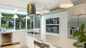 A modern kitchen with a central island, stainless steel appliances, and a view of greenery outside. - Lake 54 - Beautiful Views, Perfect Location! (Merimbula)