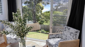 A room with a large window, a view of a garden, and a white floral arrangement on a table.
