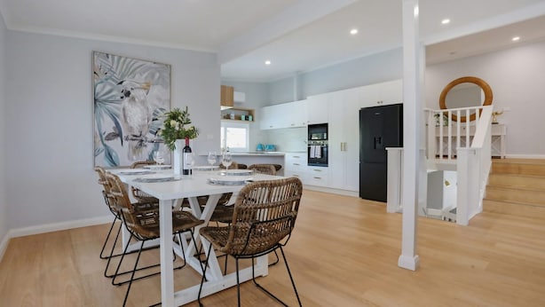 A modern kitchen with white cabinets, a black refrigerator, and a dining area with wicker chairs and a white table.