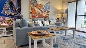 Een moderne woonkamer met een grijze bank, een salontafel en een groot abstract schilderij aan de muur.