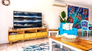 Un salon doté d’un grand téléviseur à écran plat, d’un canapé bleu, d’une table basse en bois et d’un tableau abstrait aux couleurs vives accroché au mur.