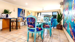 Un coin repas avec des chaises turquoise, une table et une vue sur l’extérieur.