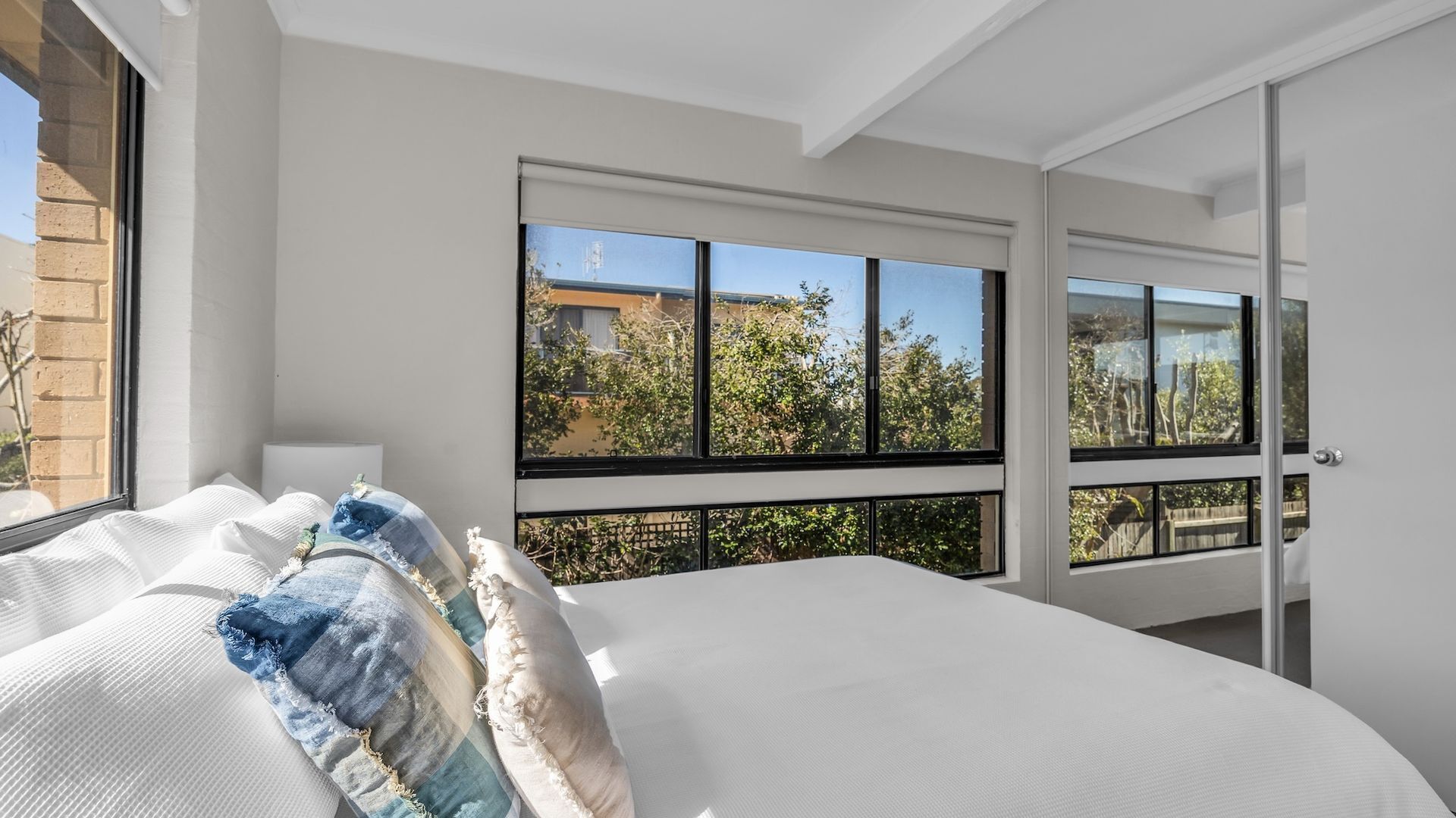 A bedroom with a large bed, multiple windows, and a view of the outside.