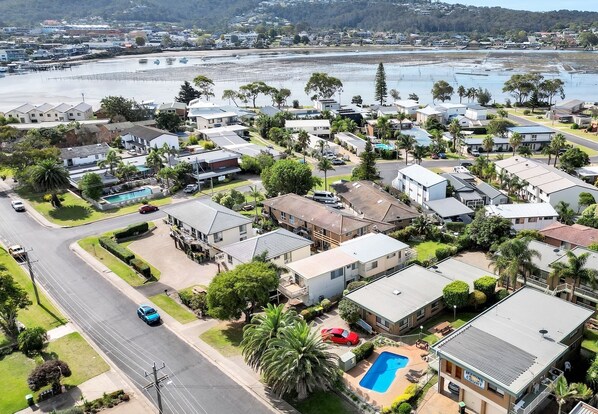 An aerial view of a residential area with houses, a swimming pool, and a marina in the background.