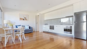 Cocina moderna con armarios blancos, electrodomésticos de acero inoxidable y un comedor con sillas de mimbre y sofá azul.