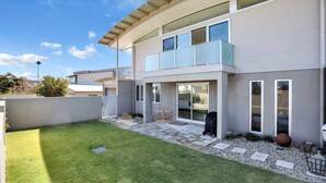 Una casa moderna de dos pisos con techo plano, ventanas amplias y un pequeño patio trasero con césped y sendero de piedra.