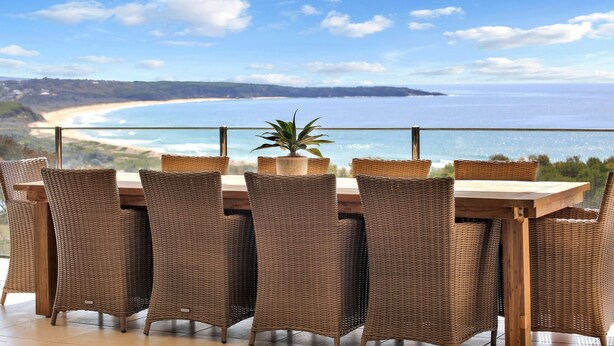 Comedor con sillas de mimbre y una mesa de madera, con vista a un paisaje costero.