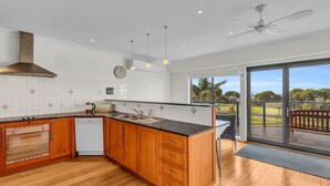 A modern kitchen with wooden cabinets, a black countertop, and a built-in dishwasher. - Our Beach House - with ocean views! (Merimbula)