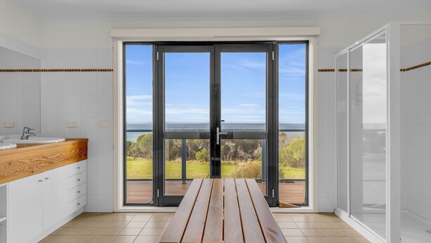 A modern kitchen with a large sliding glass door leading to a balcony with a scenic view. - Our Beach House - with ocean views! (Merimbula)