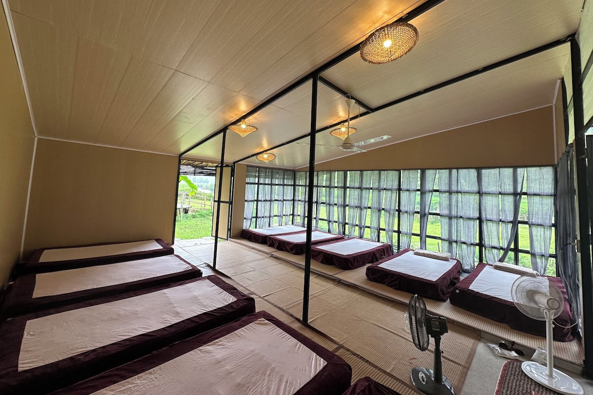Habitación con esteras de tatami, camas futón y un gran ventanal con vistas a la vegetación.