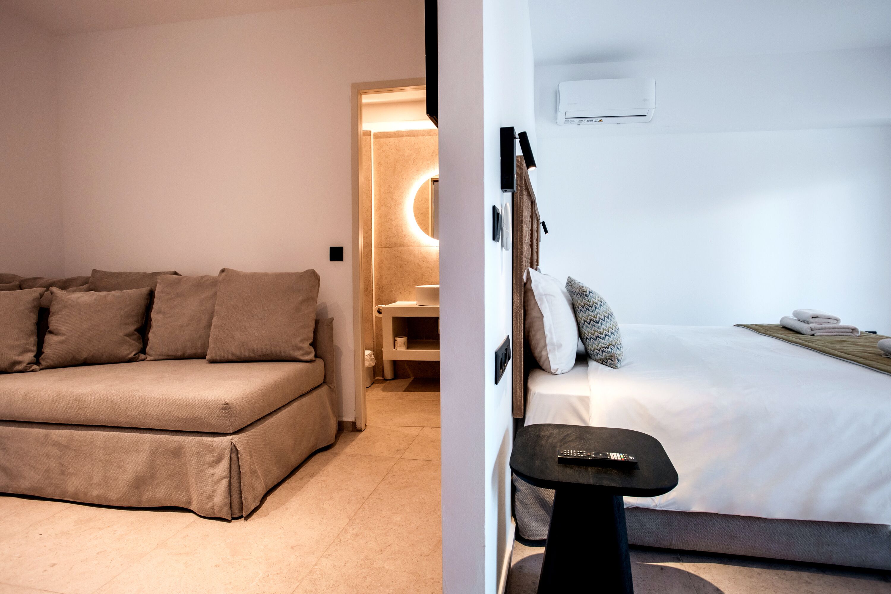 Et moderne hotelværelse med en sofa, en seng, et lille bord og en vægmonteret aircondition.