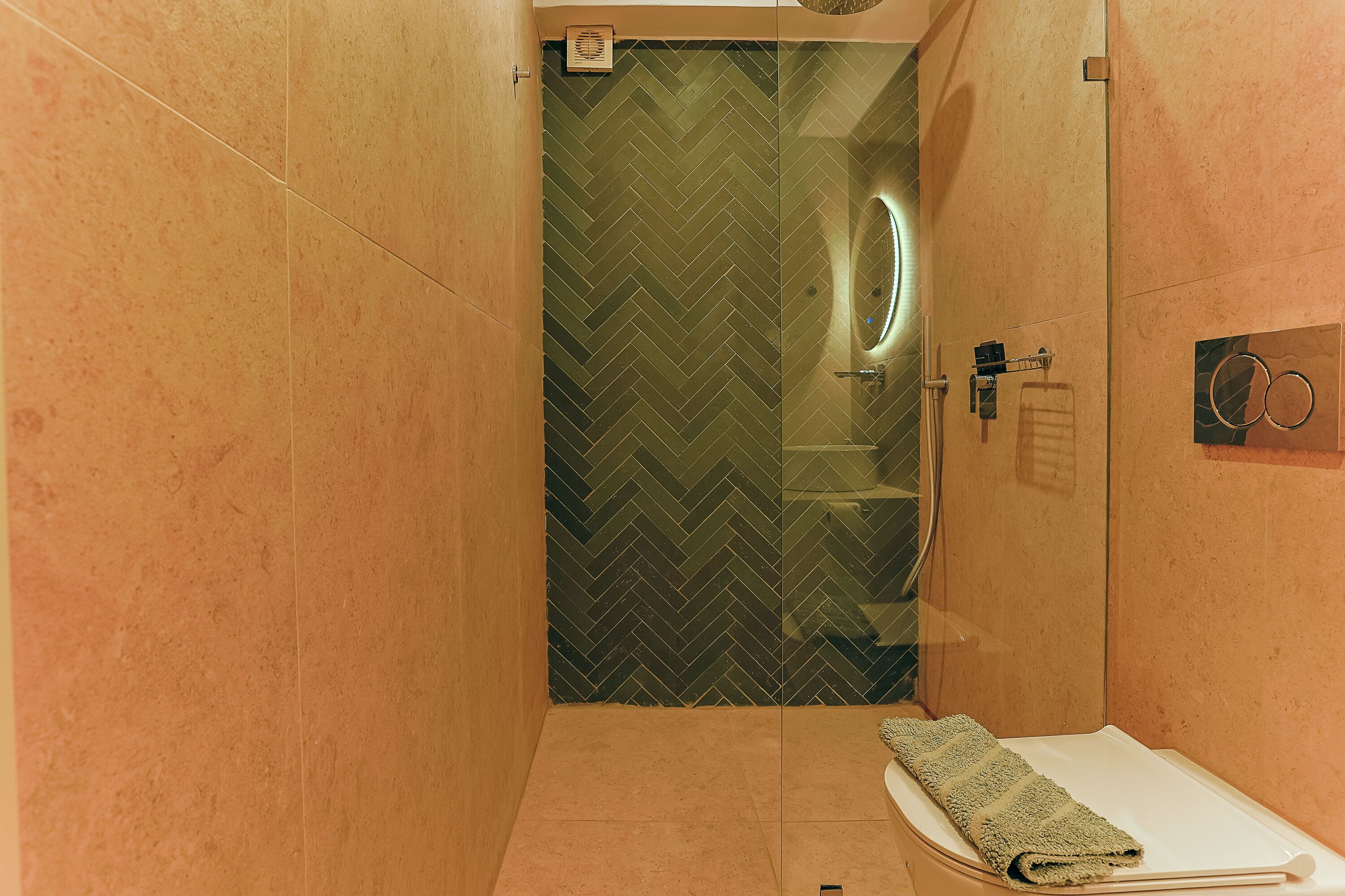 Un baño moderno con patrón de baldosas en espiga, cabina de ducha de vidrio, toallero y lavamanos pequeño.