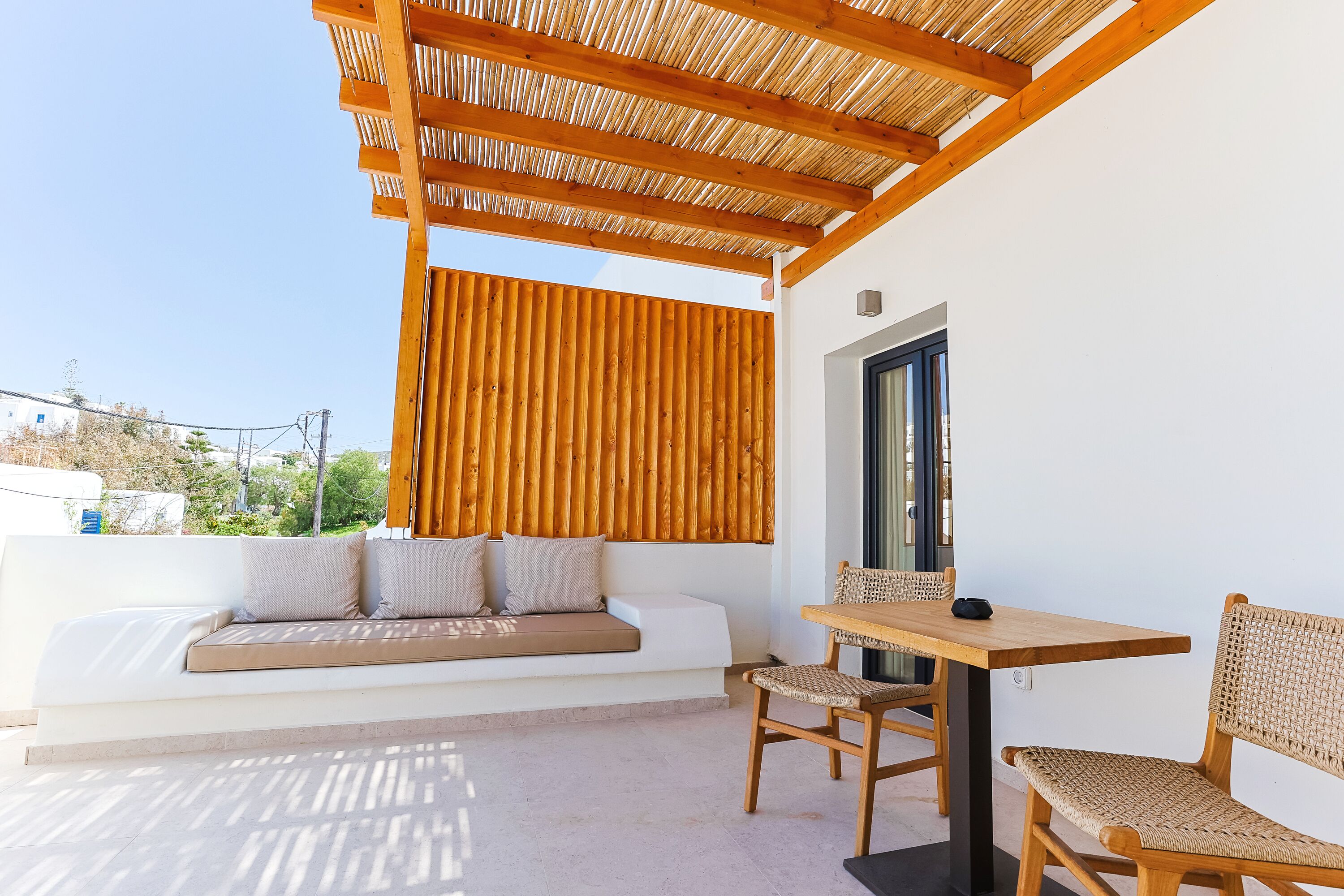 Un espace extérieur moderne, aménagé avec une table et des chaises en bois, un banc rembourré et une pergola au-dessus.