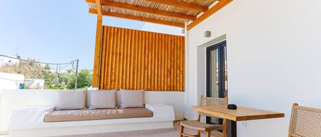 Un espace extérieur moderne, aménagé avec une table et des chaises en bois, un banc rembourré et une pergola au-dessus.
