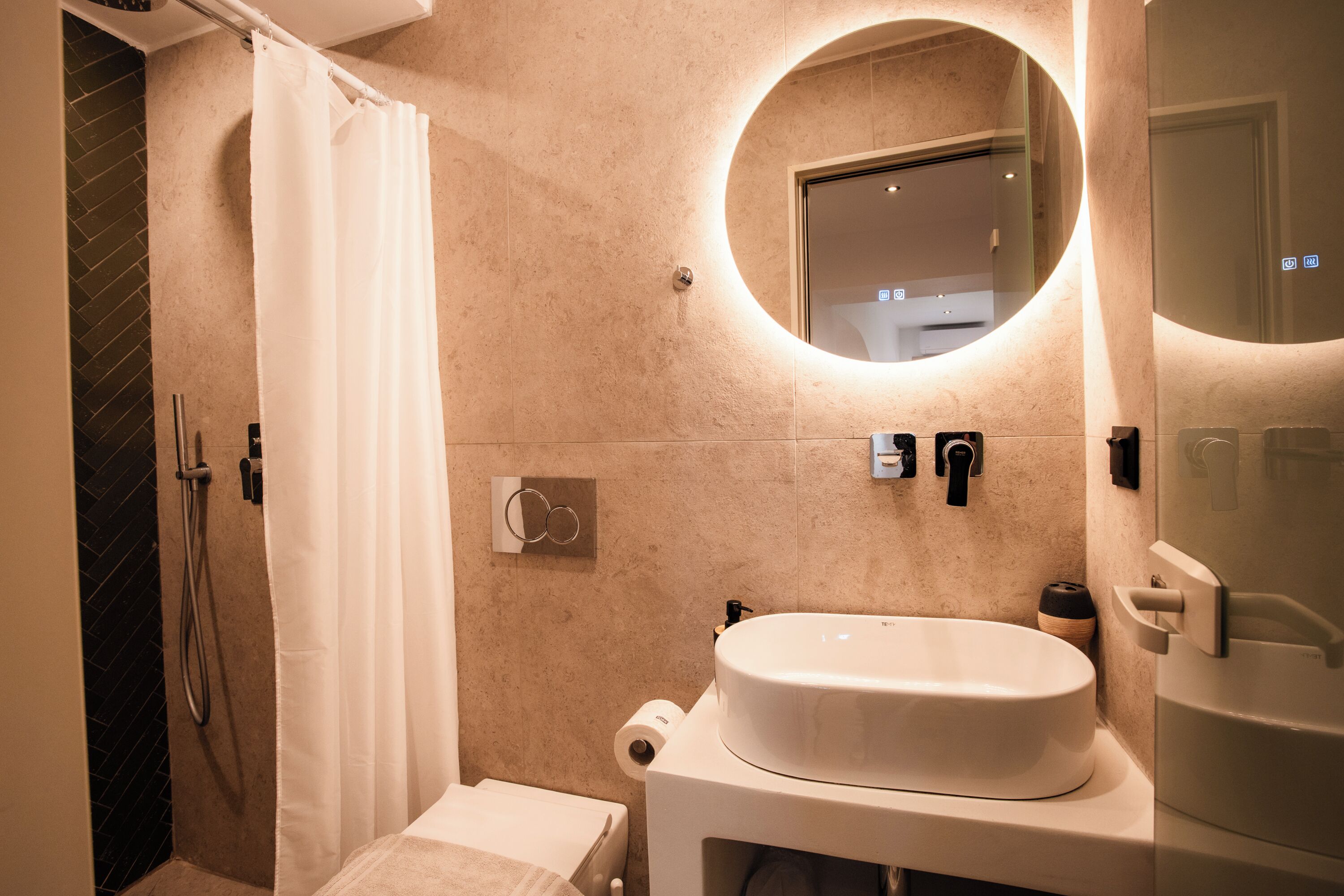A modern bathroom with a shower, toilet, sink, and a mirror with a circular light.