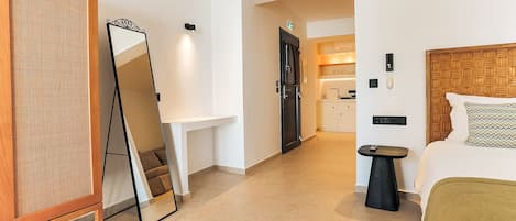 A hotel room with a large mirror, a bedside table, a bed with a headboard, and a small stool.