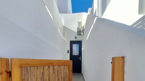 Un pasillo estrecho, con paredes blancas y una puerta al final, protegida por un portón de madera.