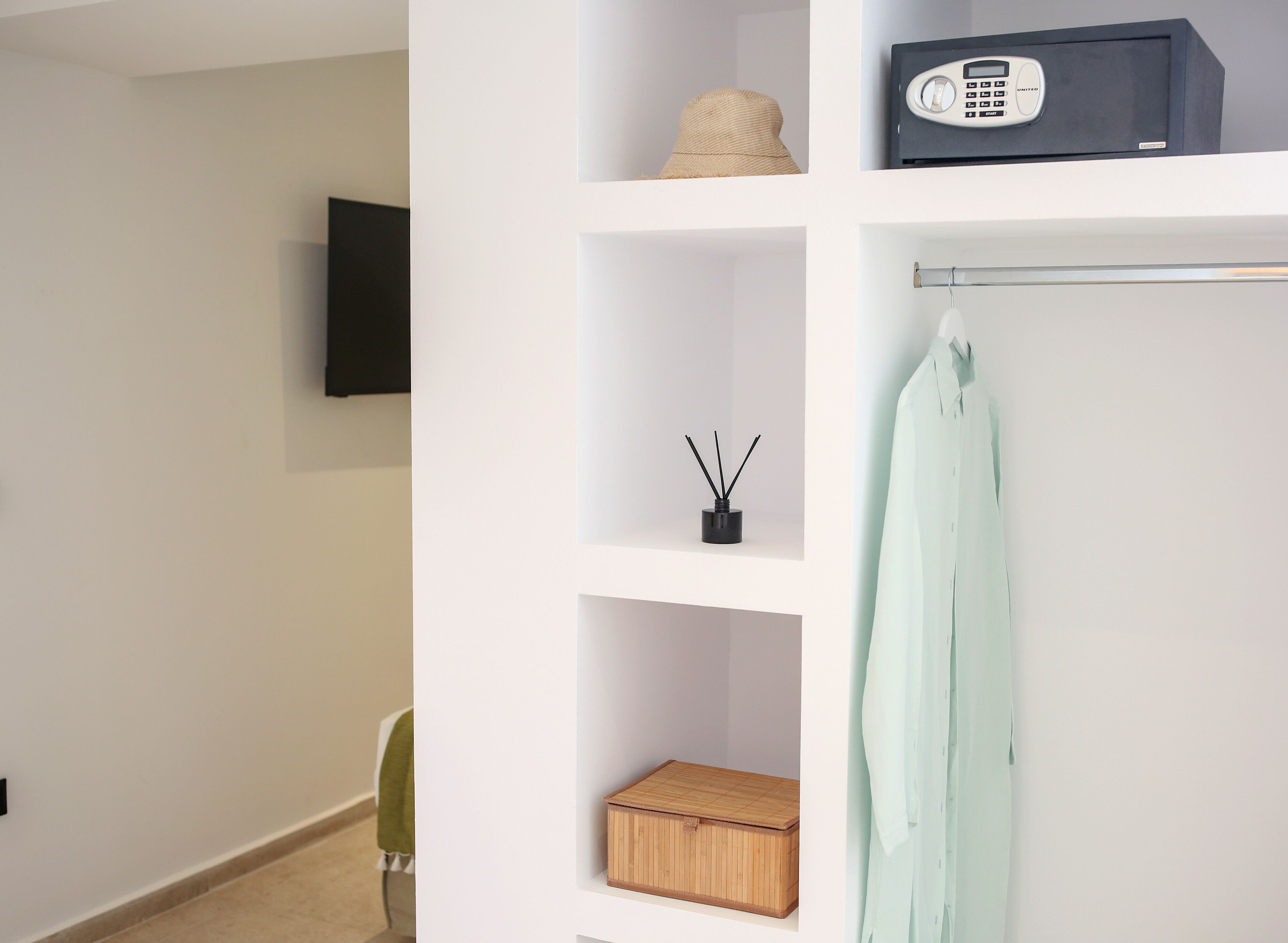 A modern, minimalist bathroom with white walls, a wooden cabinet, a bamboo box, a hat, a radio, and a towel rack.
