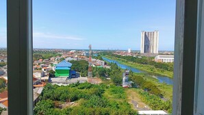 A view of a cityscape with a river, a tall building, and a green-roofed structure. - PLUM Dreamscape Bale Hinggil Surabaya (Surabaya)