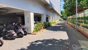 A covered parking area with multiple motorcycles parked, a paved walkway, and a row of potted plants along the right side. - PLUM Dreamscape Bale Hinggil Surabaya (Surabaya)
