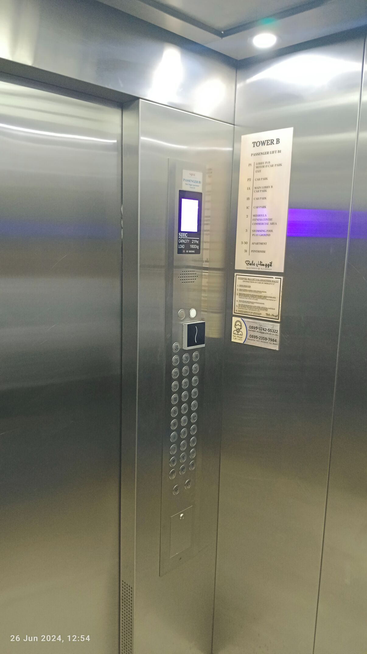 Um elevador com visor digital, números de contato de emergência e lista de andares.